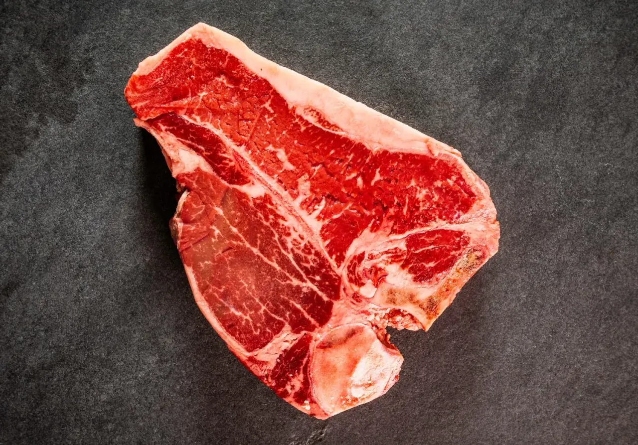 Una succulenta bistecca di manzo T-bone, con la sua marmorizzazione di grasso, pronta per essere cucinata su una superficie scura.