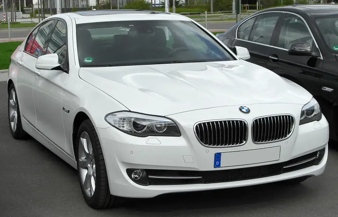 Białe BMW 535d z chromowanymi detalami i przyciemnianymi szybami, zaparkowane obok czarnego samochodu.