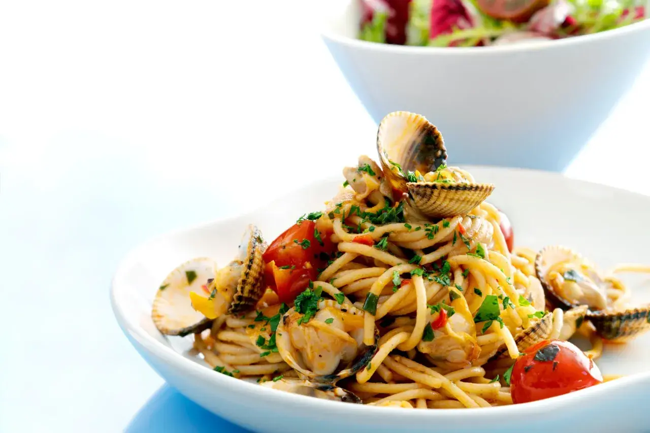 En tallrik med spaghetti vongole, toppad med färska musslor, körsbärstomater och persilja. En härlig italiensk rätt.