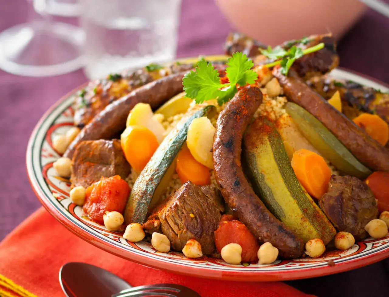 Un plat généreux de couscous royal, garni de merguez, de morceaux de viande, de légumes et de pois chiches, prêt à être dégusté.
