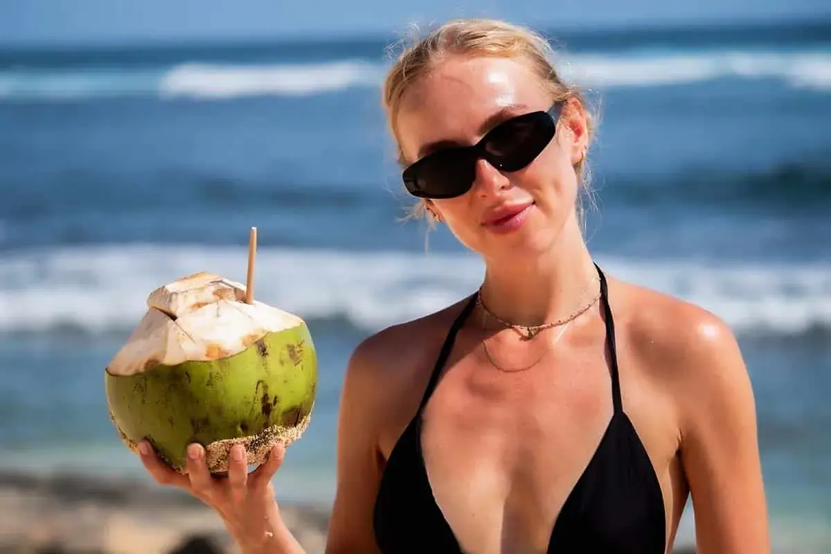 Kobieta w czarnym bikini trzyma kokosa na plaży. Idealne wakacje na Bali!