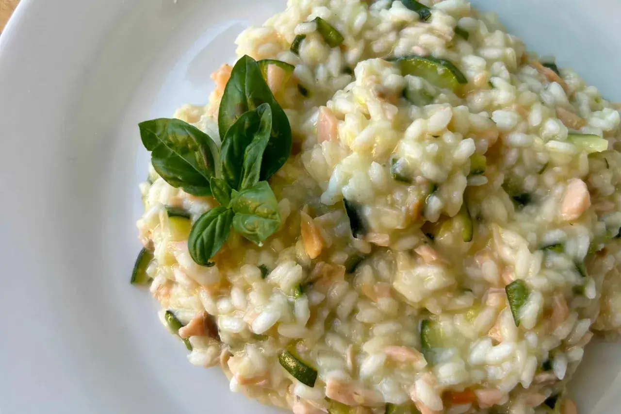Un cremoso risotto con verdure, zucchine e pezzetti di salmone, guarnito con foglie di basilico fresco.