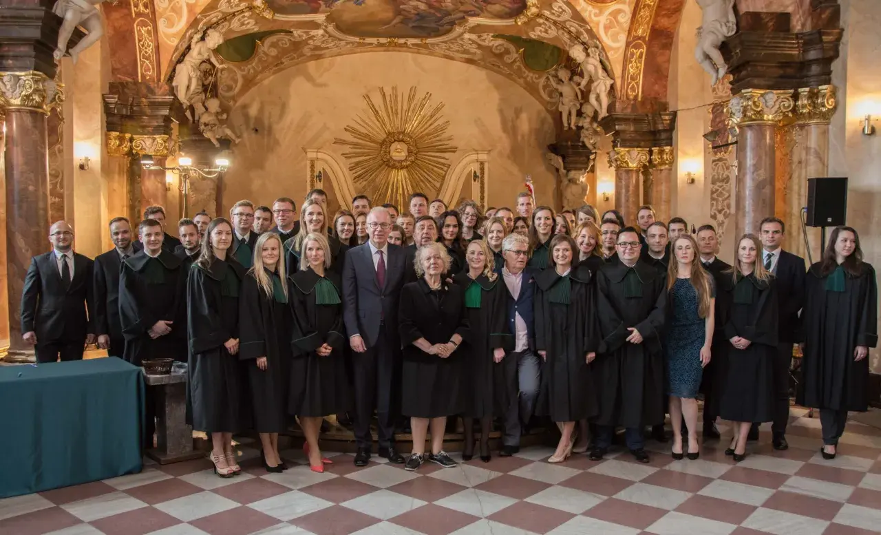 Grupa prawników w togach stoi w ozdobnym wnętrzu.
