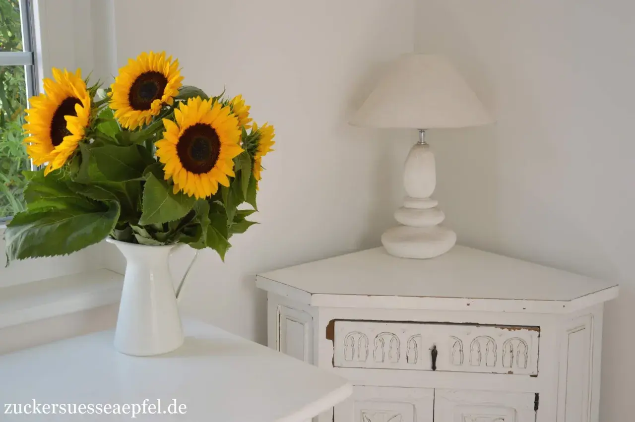 Strahlende sonnenblumen in der vase bringen Sommerstimmung in die Ecke, neben einer weißen Lampe auf einem antiken Schränkchen.