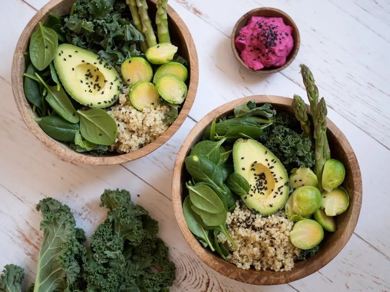 Två skålar med nyttig mat: quinoa, spenat, grönkål, avokado, brysselkål och sparris. En liten skål med rosa röra.