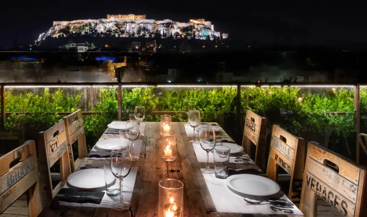 Gedeckter Tisch mit Blick auf die beleuchtete Akropolis bei Nacht.