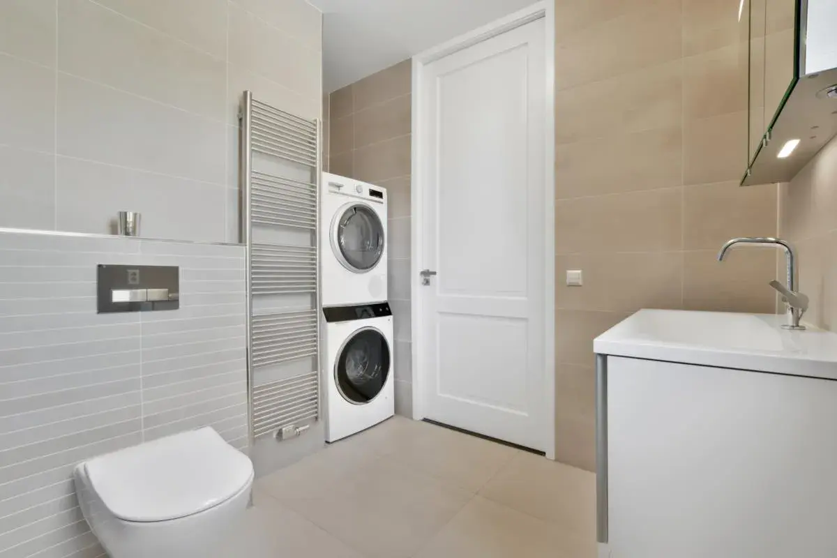 Bagno moderno con lavatrice e asciugatrice impilate, un termoarredo, un WC e un lavabo. Soluzione salvaspazio per nascondere lavatrice in bagno.