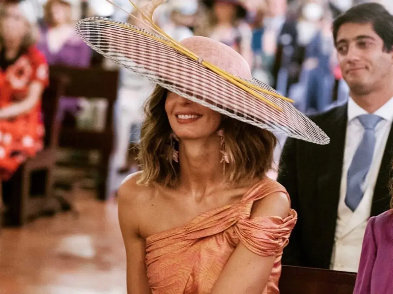 Peinado ondas invitada boda: mujer con sombrero de ala ancha y vestido naranja, sonriendo.