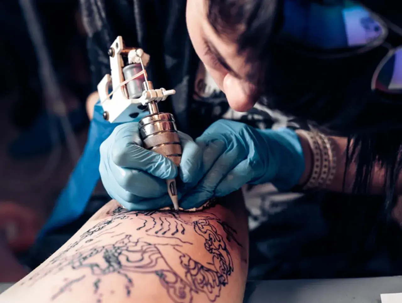 Artista creando un tatuaje de arte negro en la pierna.