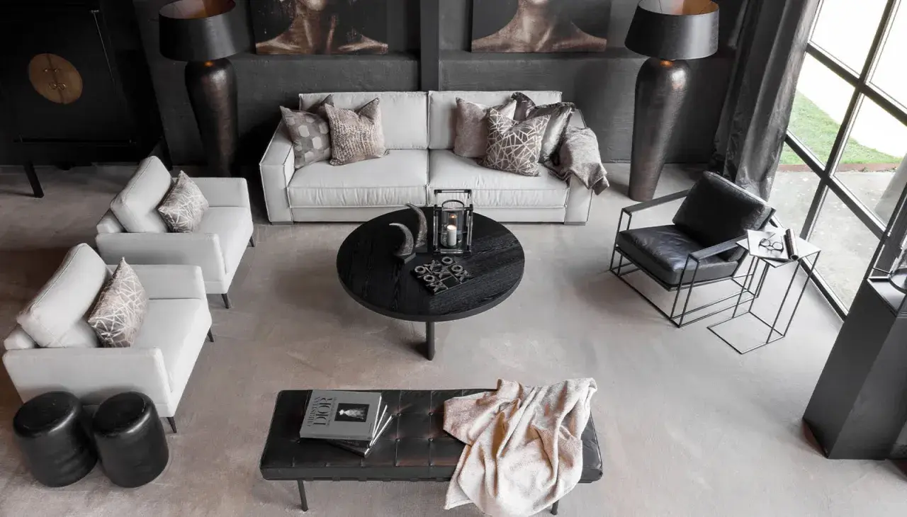 En modern lounge med soffa, fåtöljer och ett runt soffbord. En stilren och maskulin inredning med fokus på mörka toner och geometriska former.
