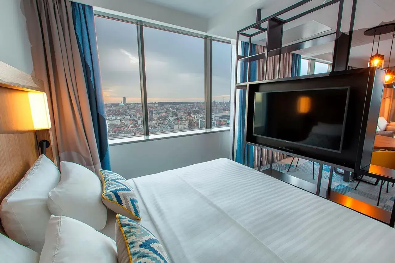 Pokój w hotelu Courtyard w Katowicach z widokiem na miasto. Łóżko, telewizor i zasłony.