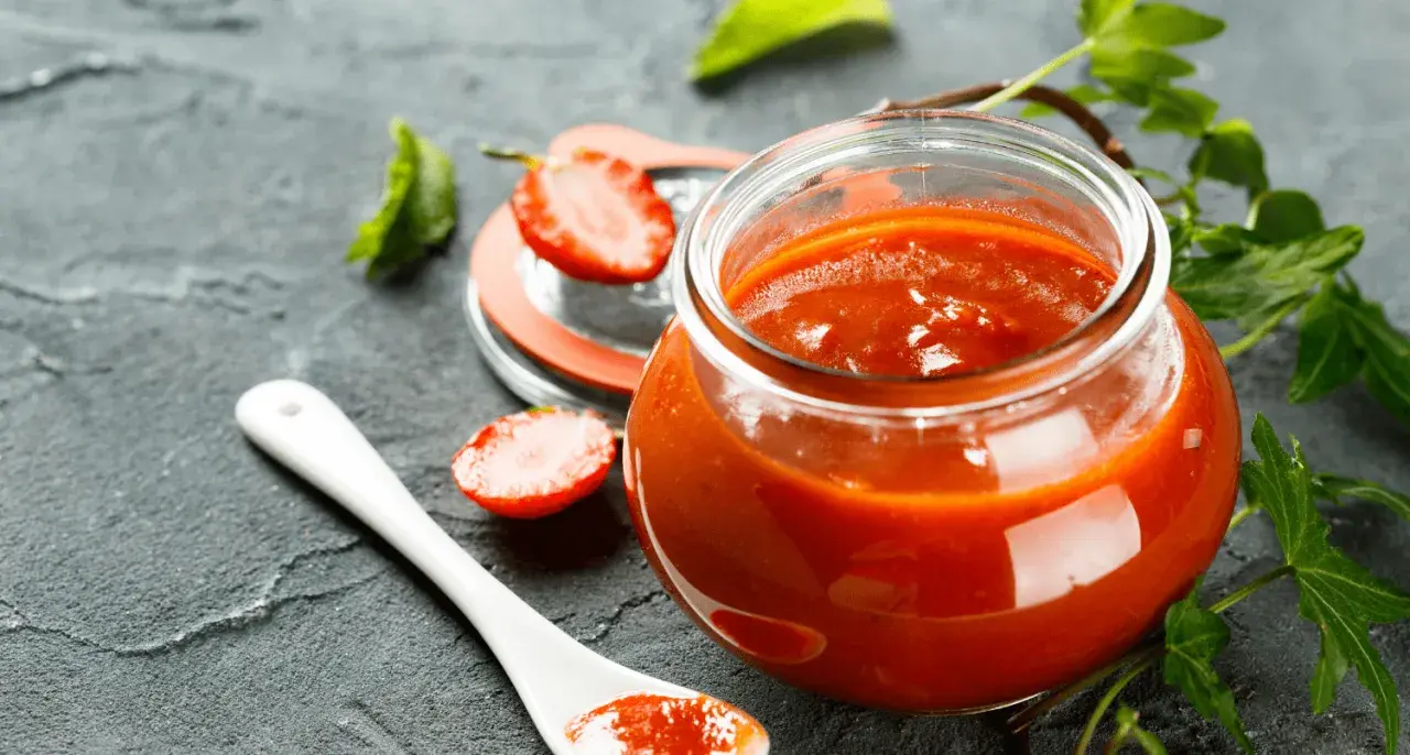 Un pot de ketchup maison, garni de fraises et de feuilles vertes, sur fond sombre.