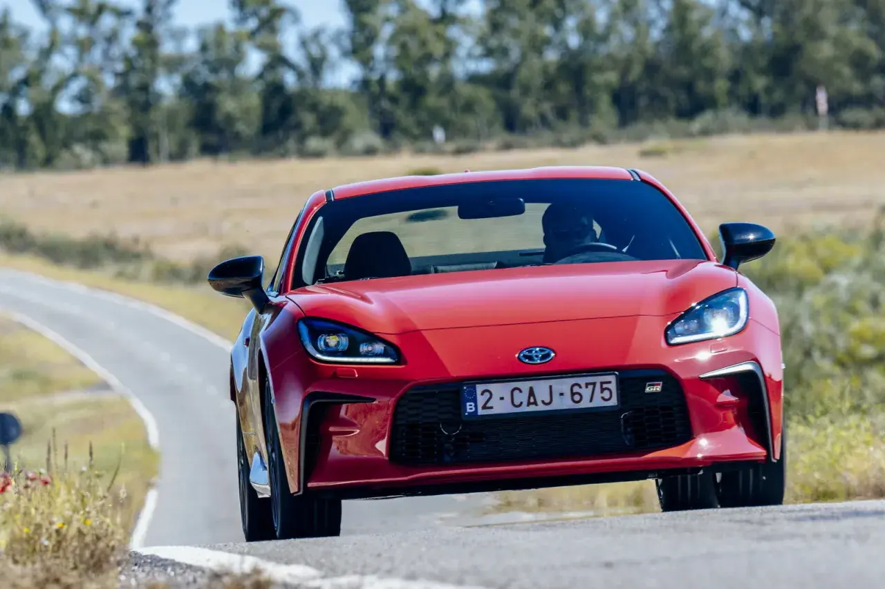 La Toyota sportiva rossa sfreccia su una strada tortuosa, con il sole che illumina il suo design aggressivo.