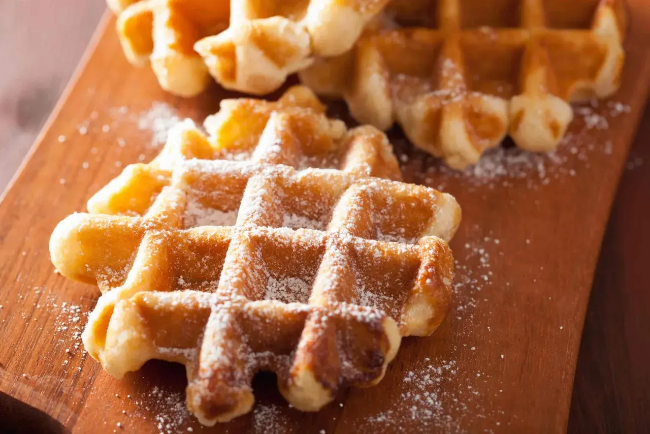 Gaufres liégeoises dorées saupoudrées de sucre glace sur une planche en bois. Un délice croustillant.