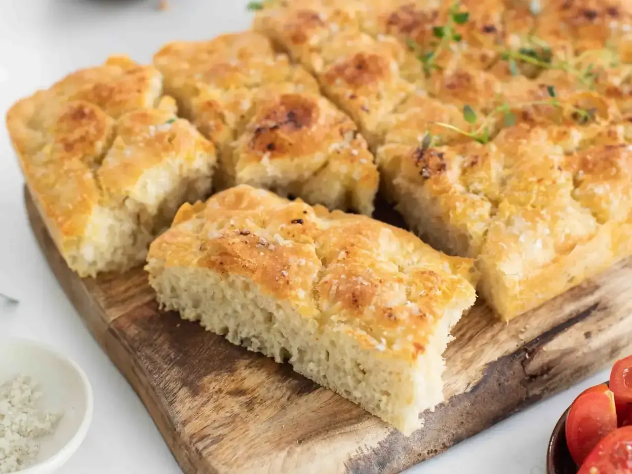 Focaccia dorada y tierna con sal gruesa y romero, cortada en porciones sobre tabla de madera.