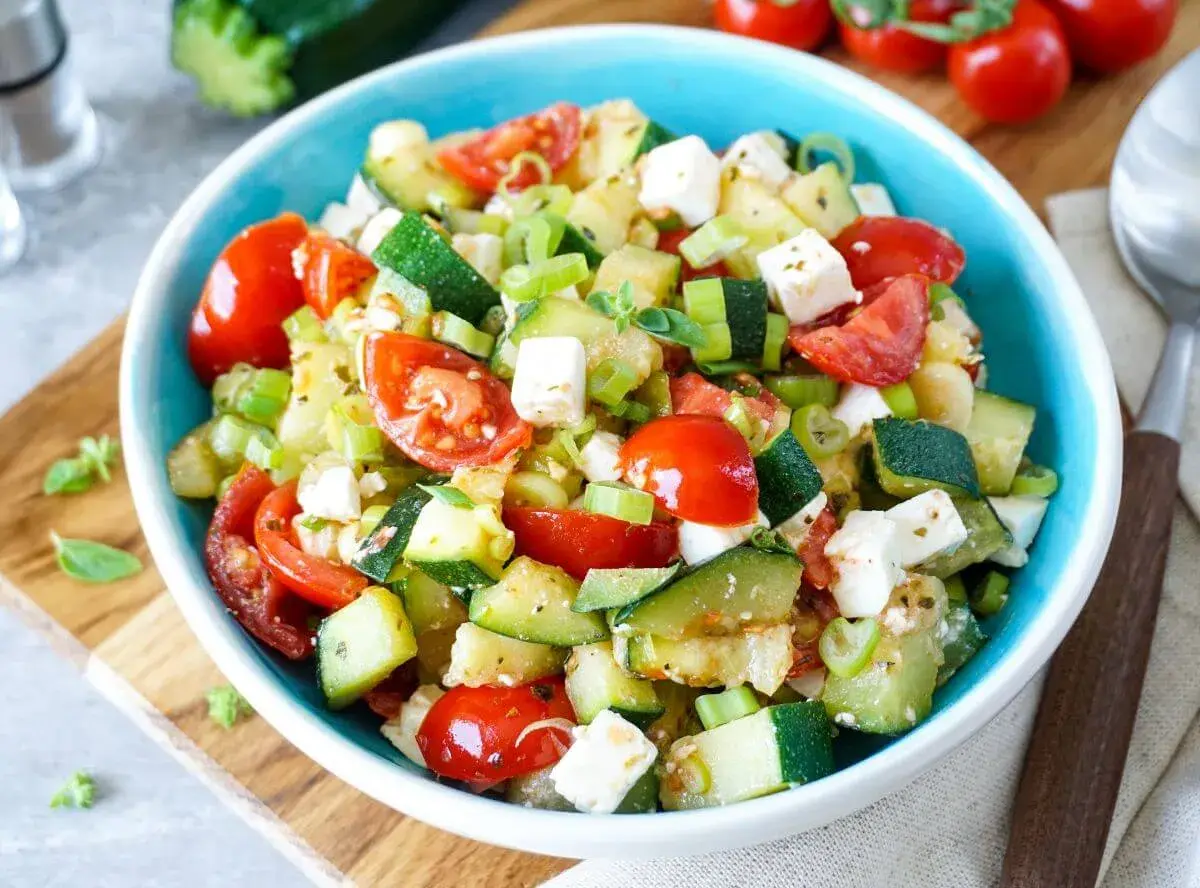 Frischer Zucchini Salat mit Tomaten, Feta und Frühlingszwiebeln in einer blauen Schüssel. Ein leichter Genuss!