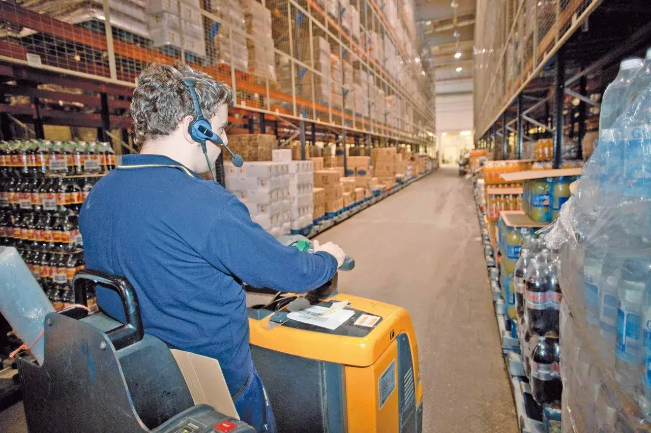 Mitarbeiter mit Headset führt Kommissionierauftrag per Sprachsteuerung (pick by voice) im Lager durch.