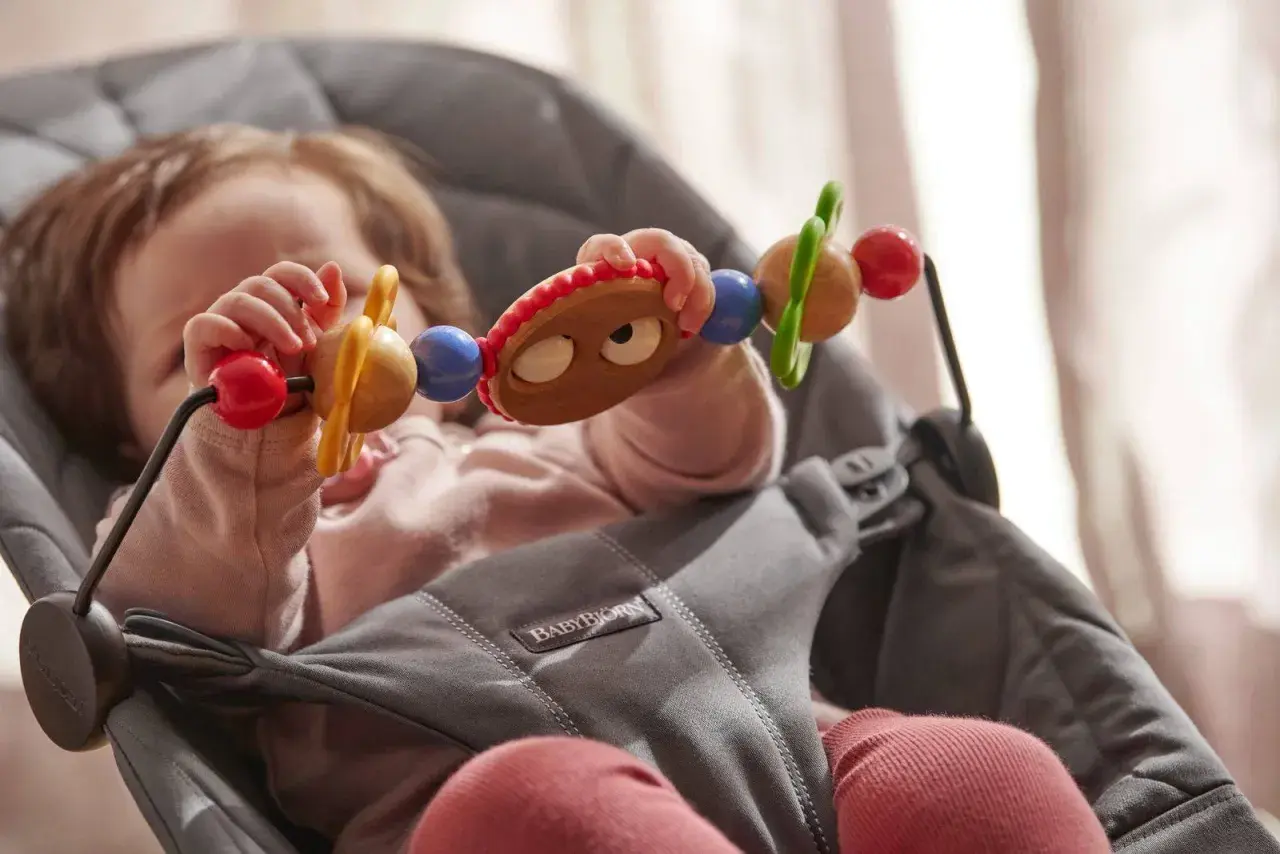 Maluch bawi się zabawką w leżaczku BabyBjorn. Od kiedy dziecko zaczyna sięgać po przedmioty, taki leżaczek jest idealny.