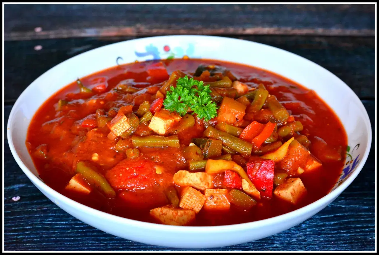 Pyszne leczo z tofu, z fasolką szparagową i papryką w sosie pomidorowym, udekorowane natką pietruszki.