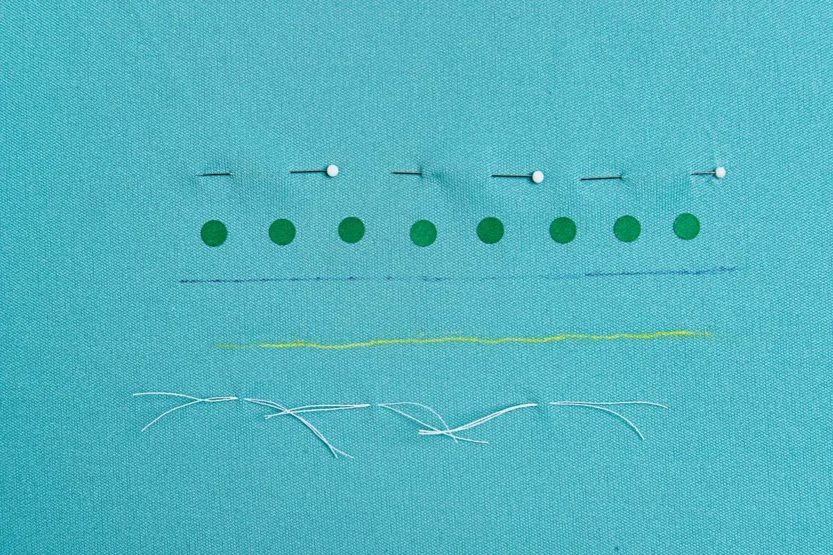 Tissu bleu turquoise avec des épingles, des ronds verts, des traits bleus, jaunes et des fils blancs.