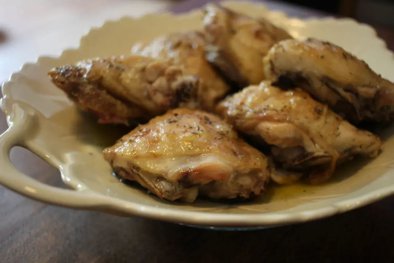 Plusieurs hauts de cuisse de poulet rôtis, assaisonnés d'herbes, reposent sur une assiette en céramique crème.