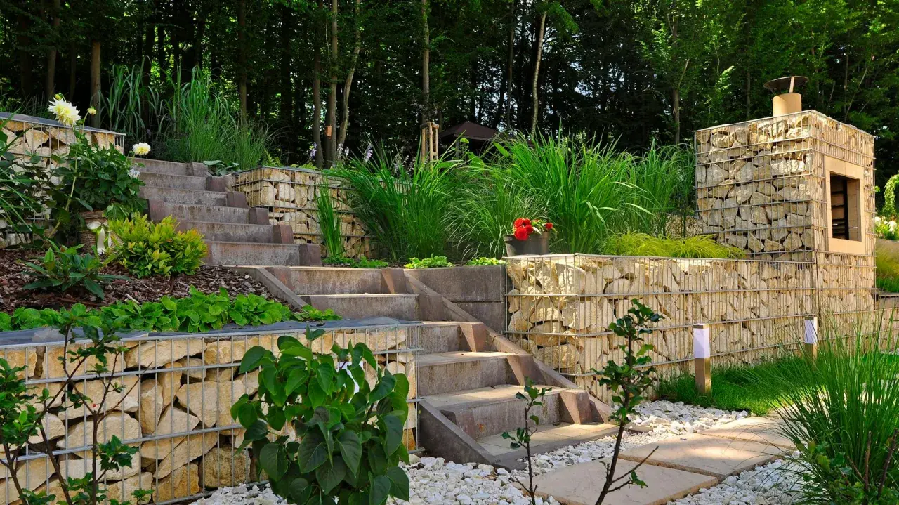 Moderne Gartenaufteilung Ideen mit Gabionenmauern, Steintreppen und üppiger Bepflanzung. Ein Kamin aus Steinen integriert sich harmonisch.