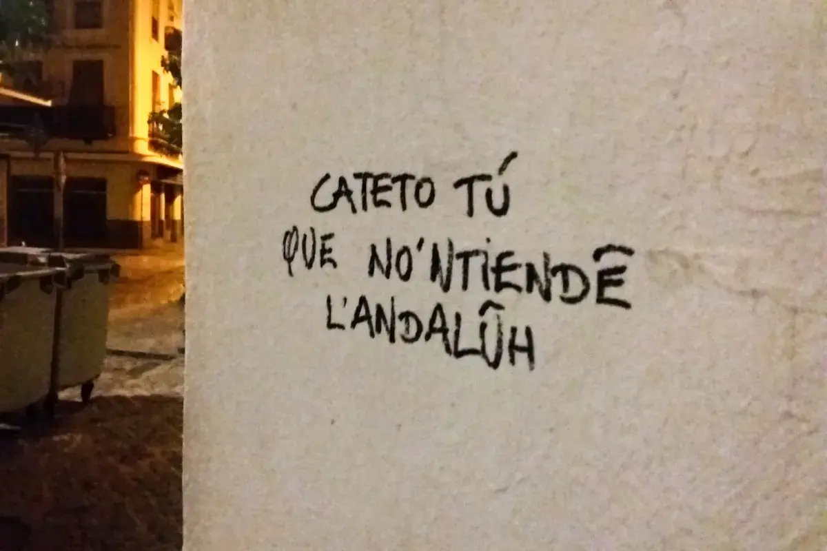 Graffiti en una pared con **expresiones sevillanas**: "Cateto tú que no'ntiende l'andalúh".