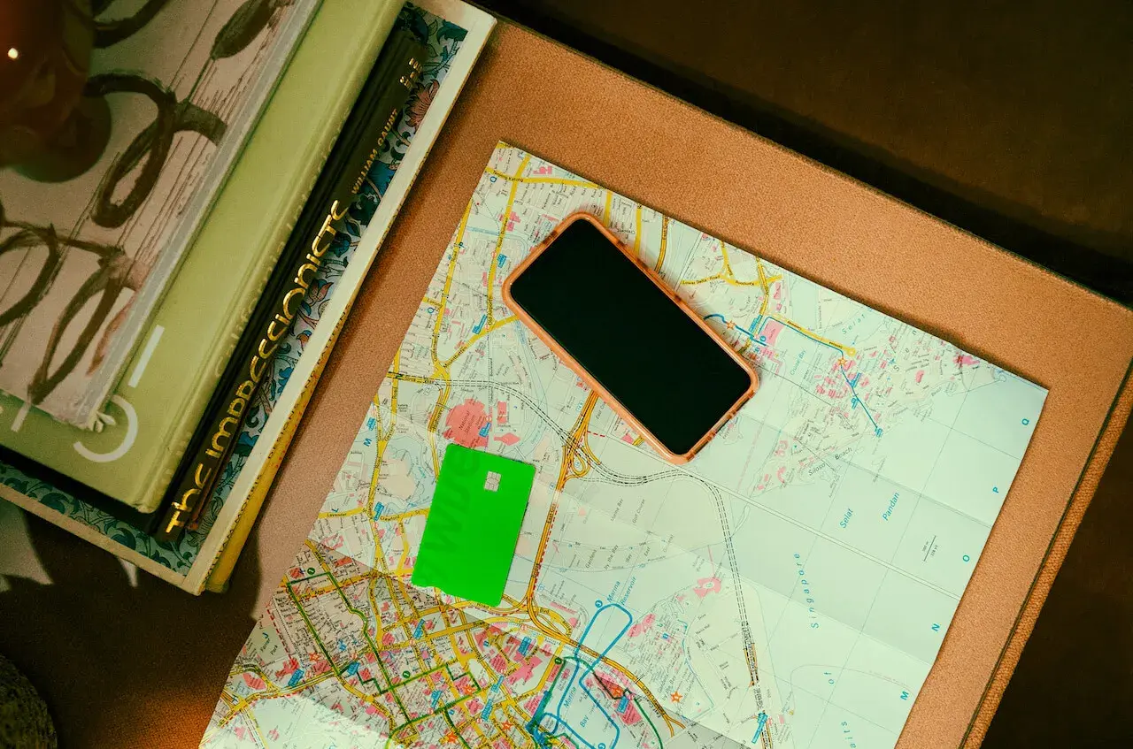 Zielona karta płatnicza, telefon i mapa leżą obok książek. Może to być przygotowanie do podróży, gdzie przyda się waluta Rumunii.