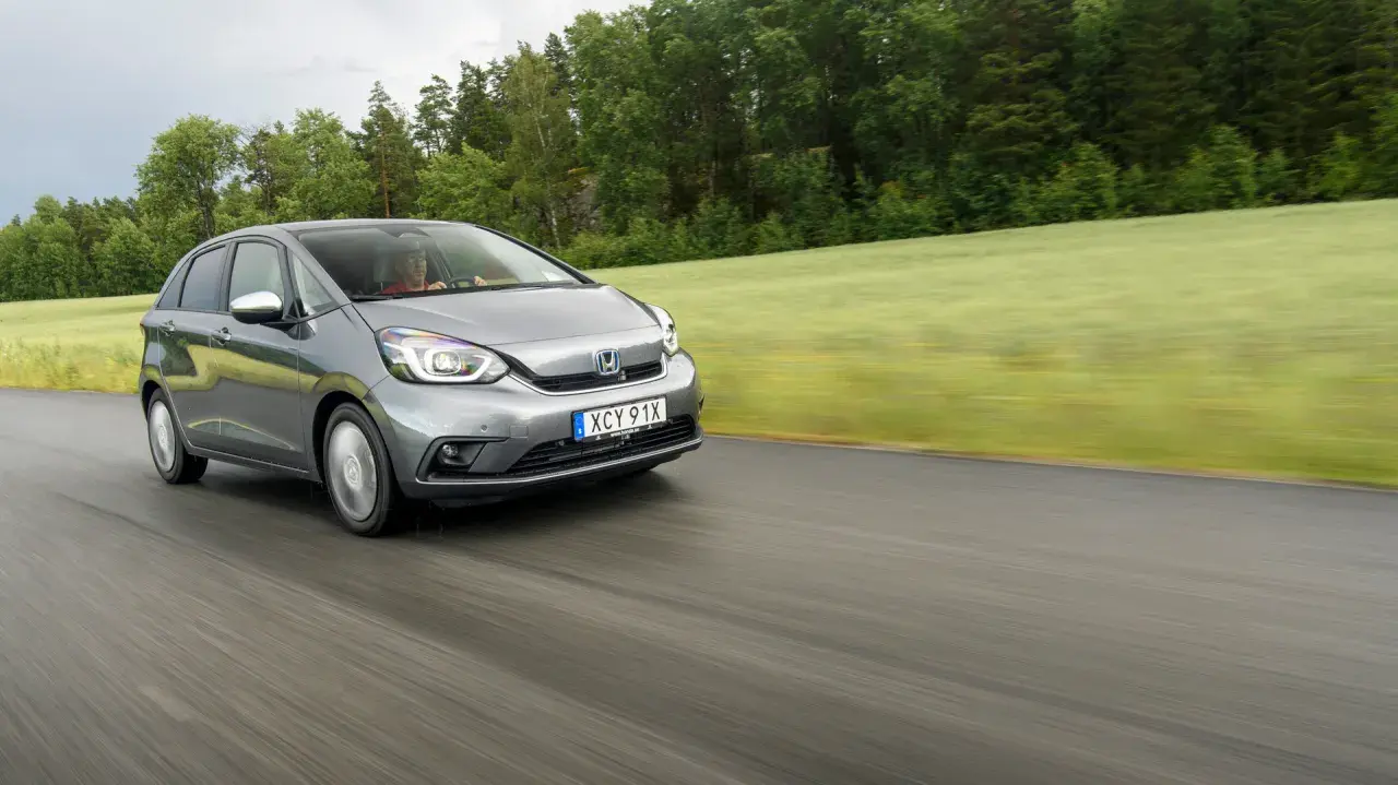 Grå Honda Jazz kör på en väg genom ett grönt landskap. Inga problem med denna bil, bara en härlig tur.