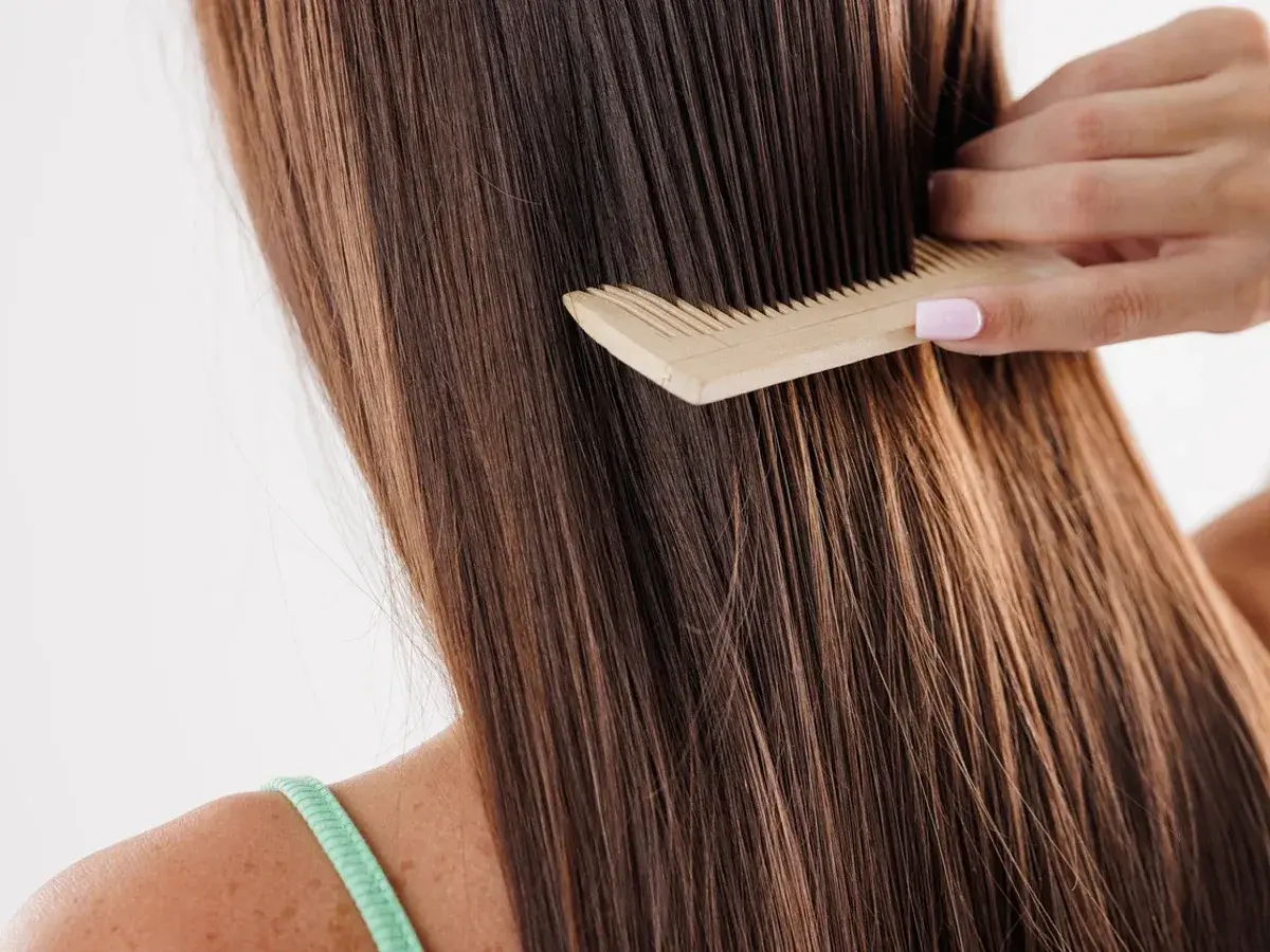 Peinando el pelo largo y castaño, que luce un poco apelmazado, con un peine de madera.