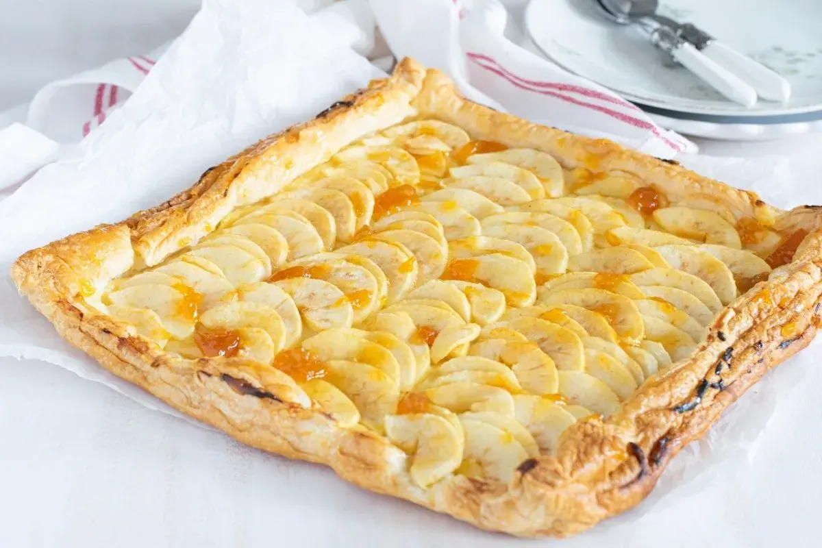 Tarta de manzana con crema pastelera, con finas láminas de manzana y un glaseado dorado sobre hojaldre crujiente.