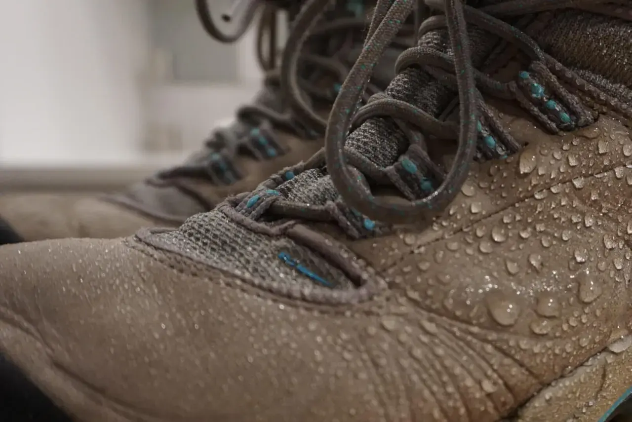 Close-up of tan hiking boots covered in water droplets, showing how to waterproof hiking boots effectively.