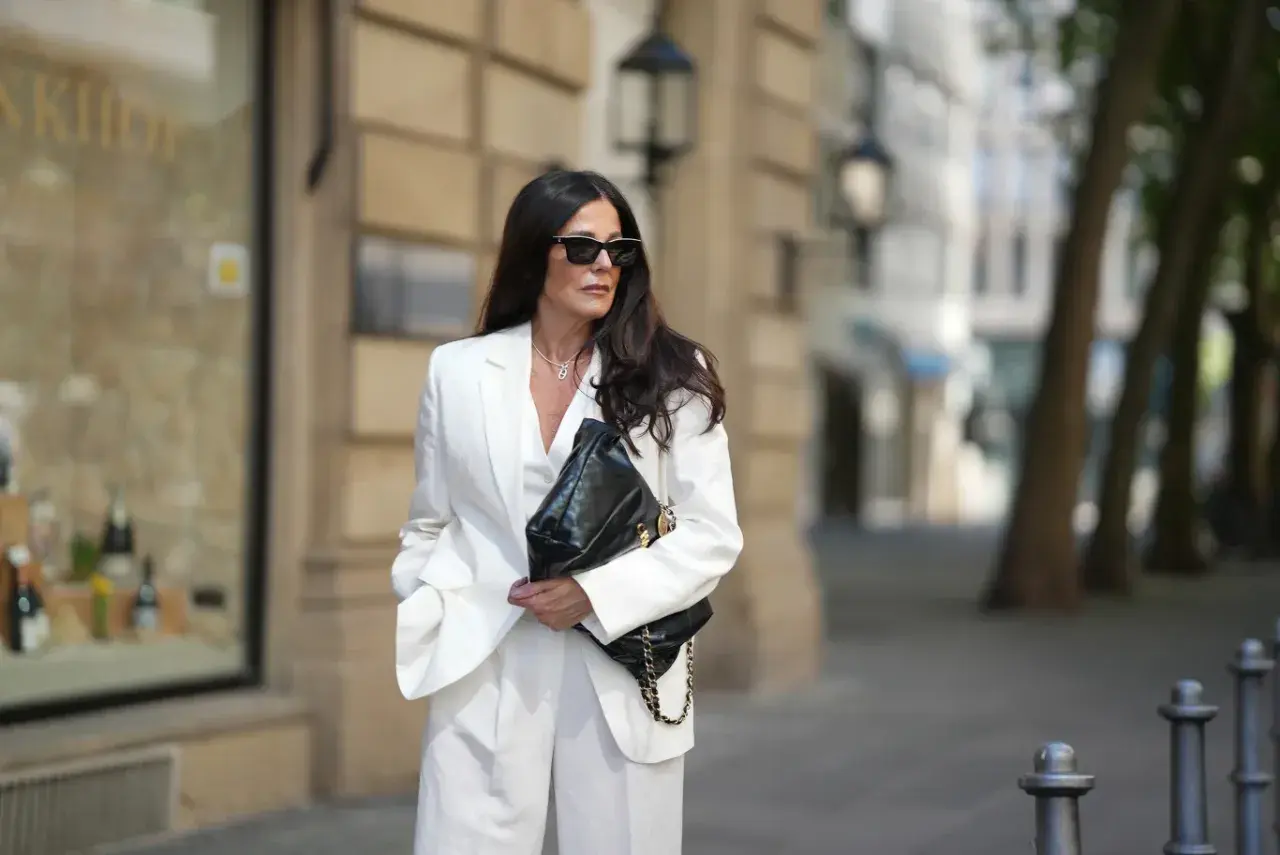 Elegancka biała stylizacja z marynarką i spodniami to świetny pomysł, jak się ubrać na komunię. Czarna torebka dodaje kontrastu.