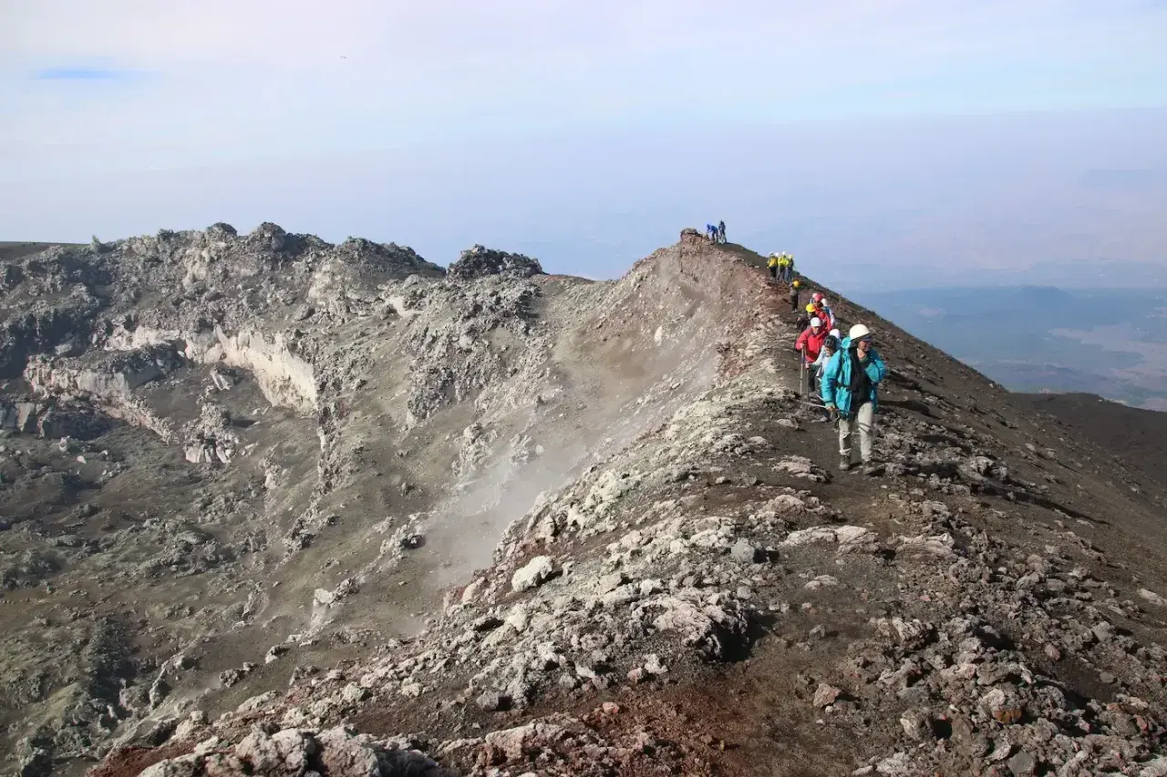 Escursionisti sul sentiero della cima Etna, tra rocce vulcaniche e fumo.