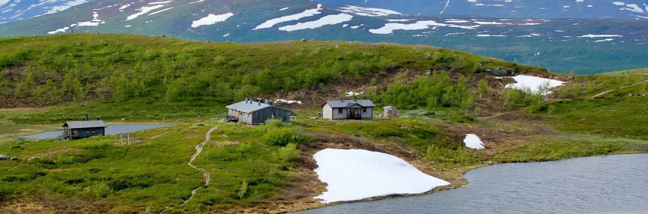 Fjällstugor längs Kungsleden nära Hemavan, med snöfläckar och gröna kullar.