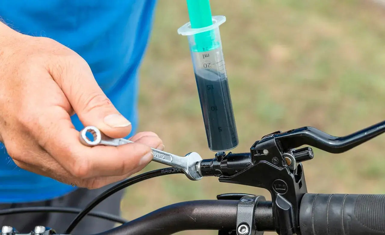 Person stellt hydraulische bremse fahrrad ein. Mit Spritze und Werkzeug wird Bremsflüssigkeit eingefüllt.