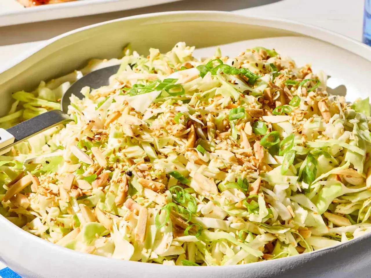 A refreshing Japanese cabbage recipe salad, topped with toasted almonds, sesame seeds, and green onions, served in a white bowl.