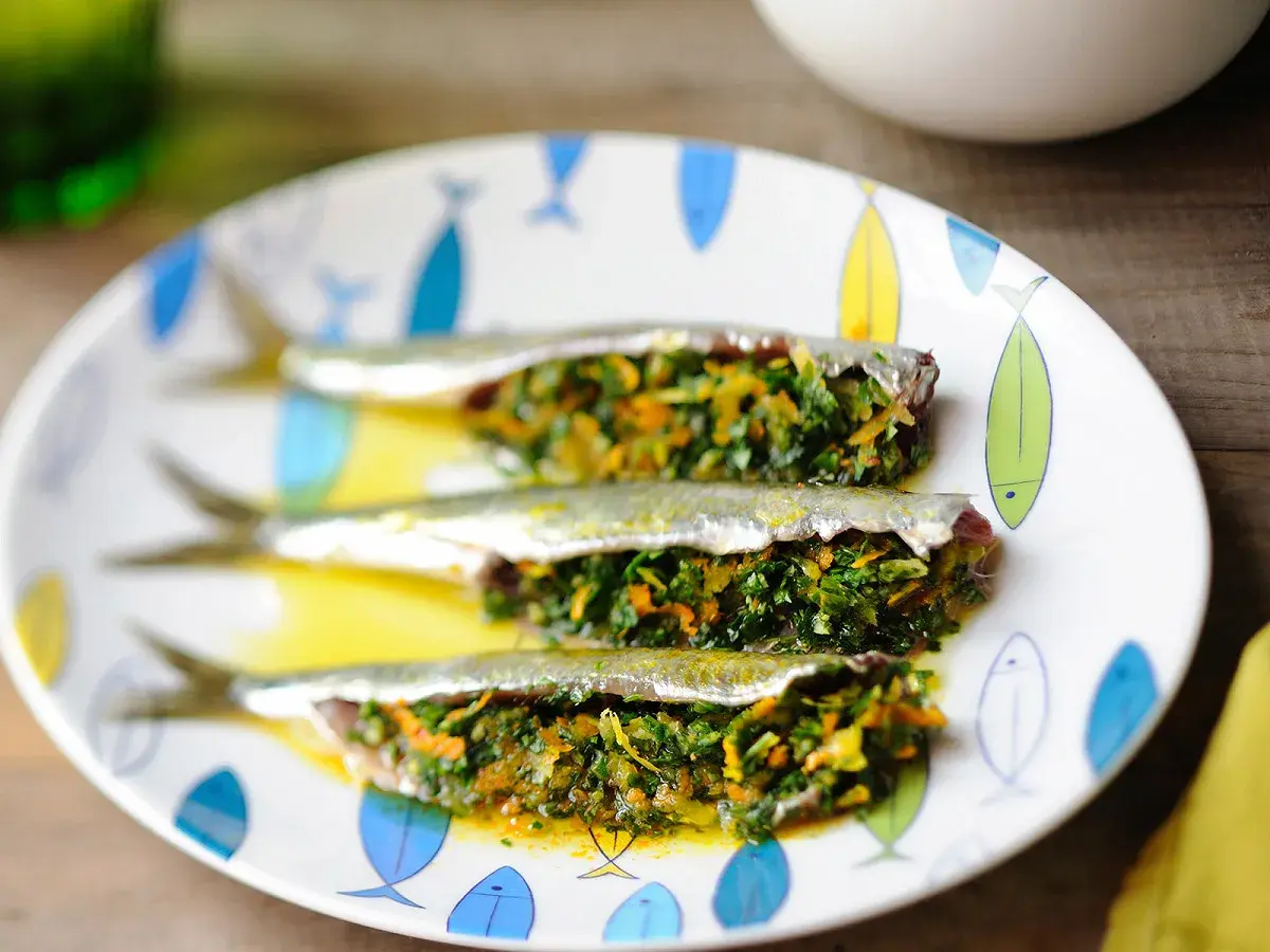 Trois sardines farcies aux herbes et légumes, servies sur une assiette décorée de poissons.