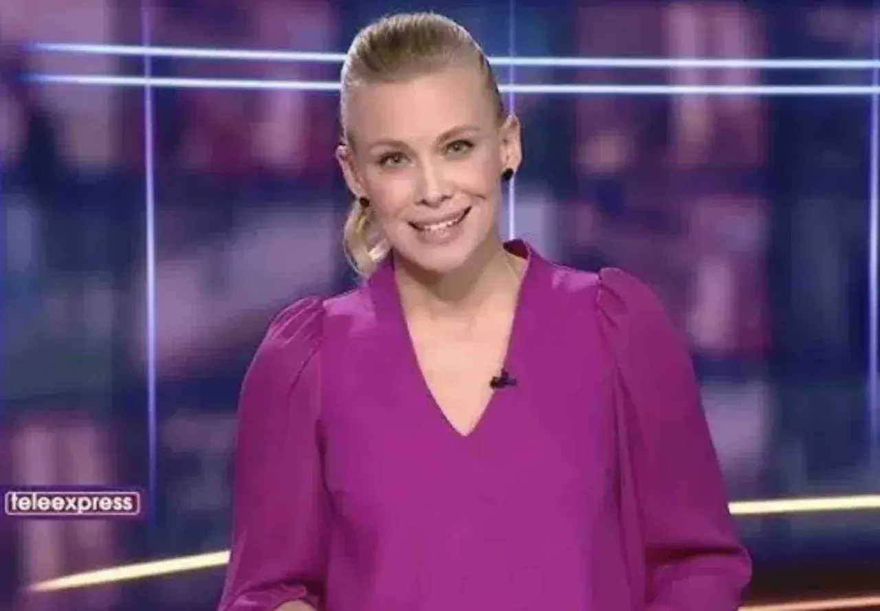 Aleksandra Kostrzewska uśmiecha się do kamery w fioletowej bluzce. W tle logo "teleexpress".