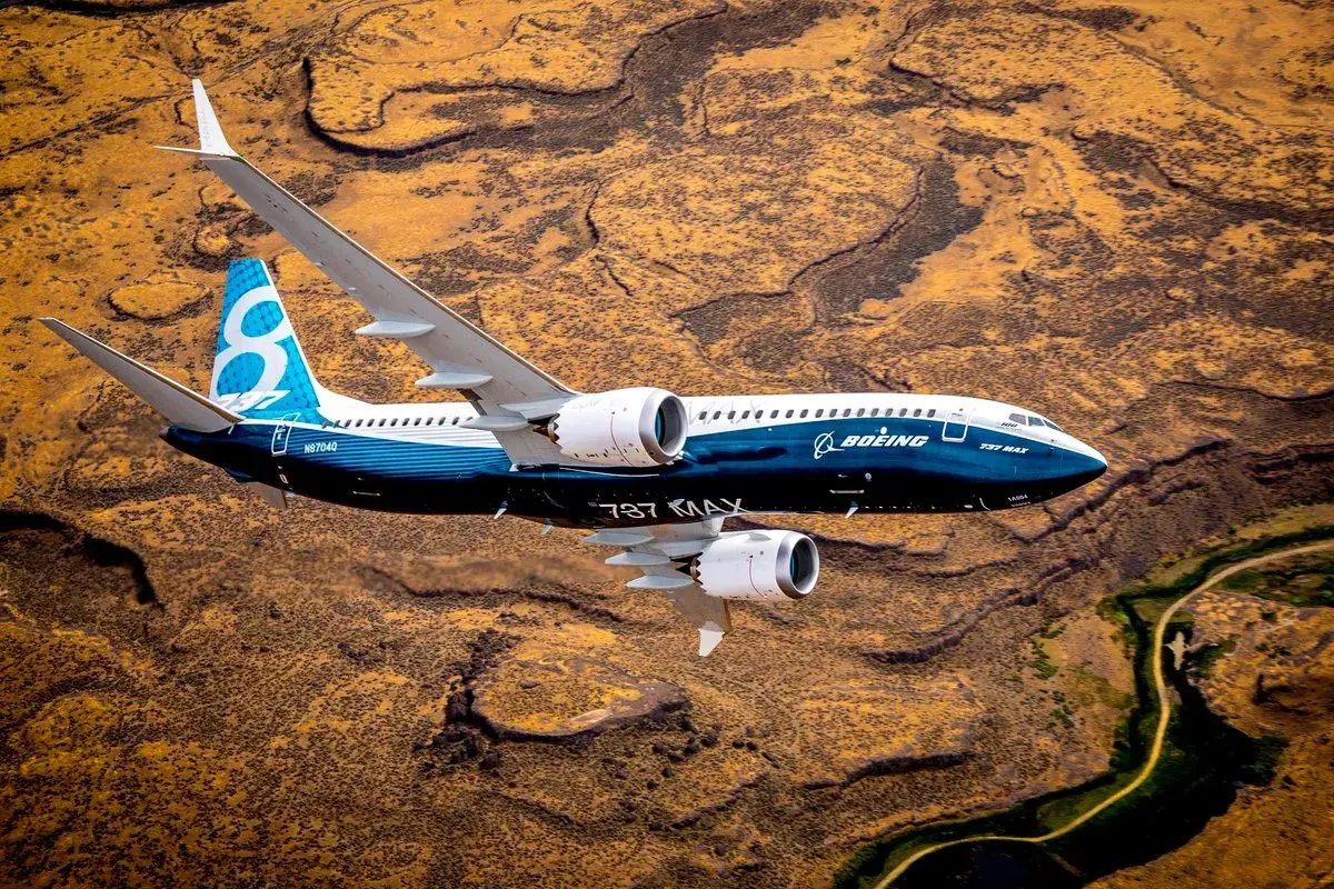Boeing 737 MAX 8-200 z niebieskim ogonem z cyfrą 8 leci nad pustynnym krajobrazem.