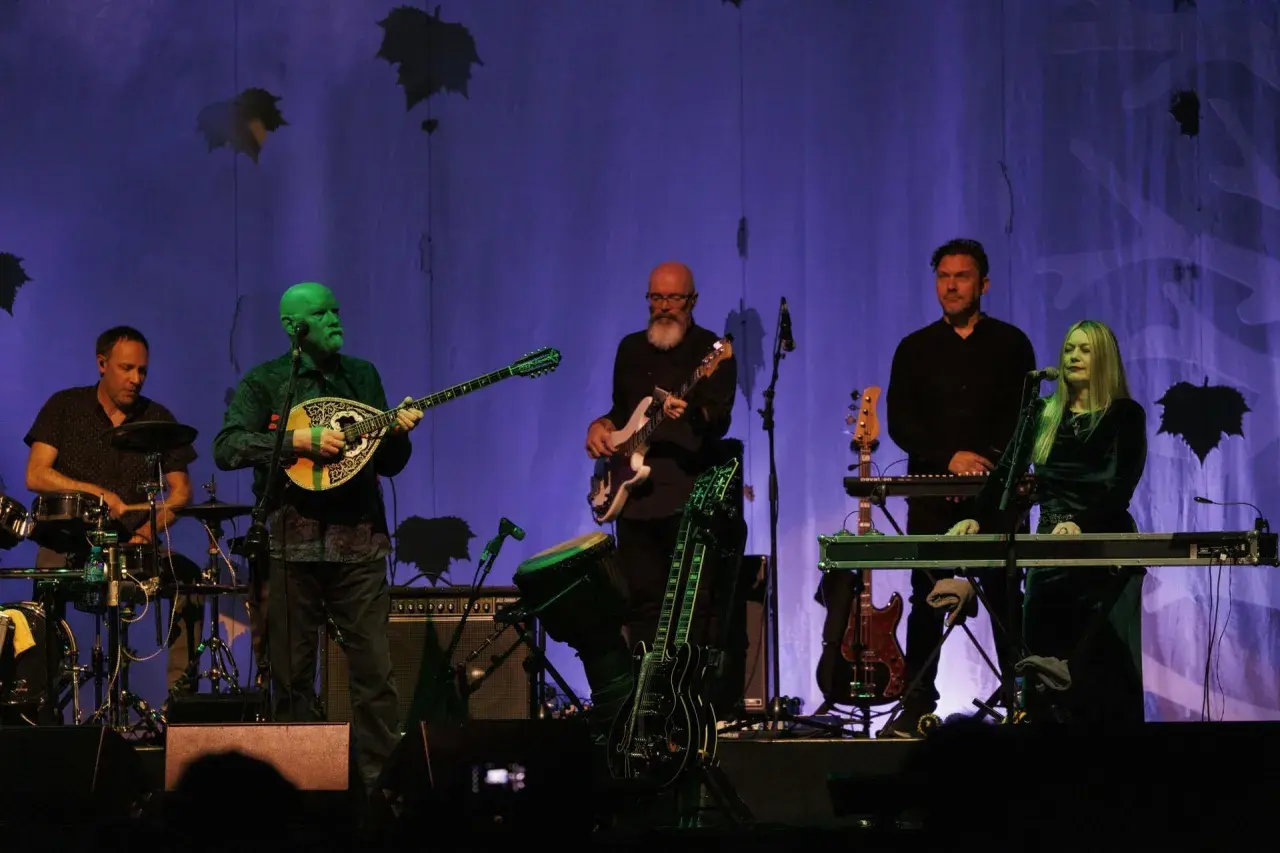 Zespół Dead Can Dance na koncercie. Muzycy grają na instrumentach, w tle fioletowa kurtyna z liśćmi.