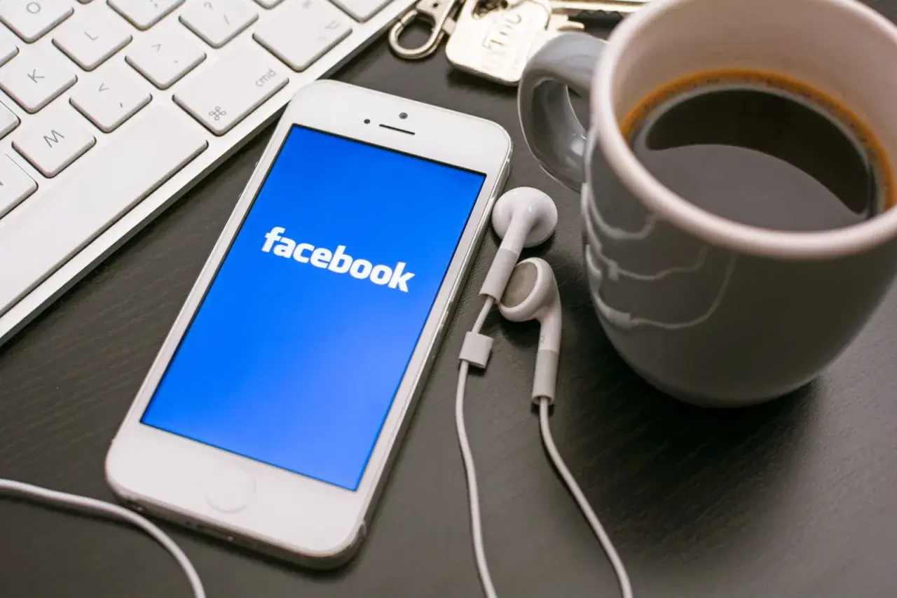 Telefon z Facebookiem, klawiatura i kawa. Dowiedz się, jak założyć konto szkoły na Facebooku, by być bliżej uczniów.