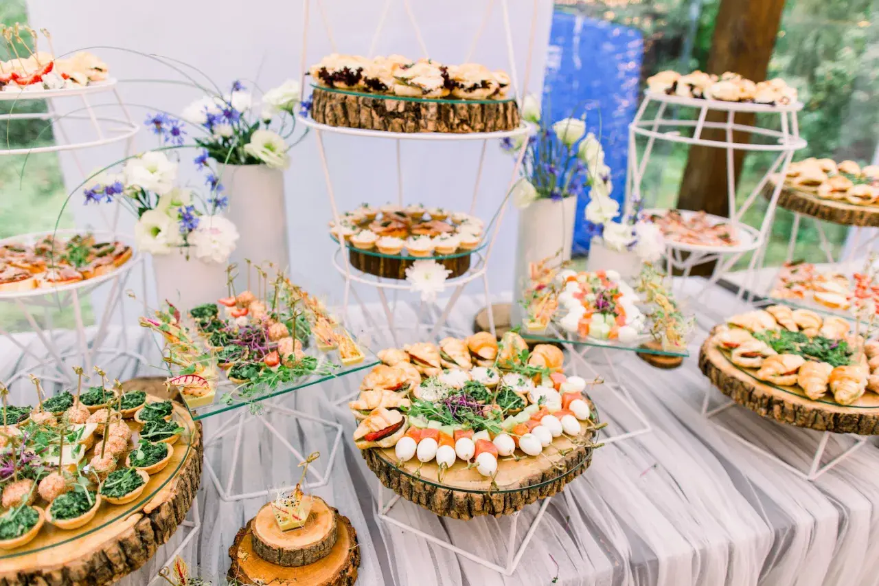 Un buffet de mariage participatif avec une variété de petits fours, tartines et brochettes, joliment présentés sur des rondins de bois et des étagères en verre.