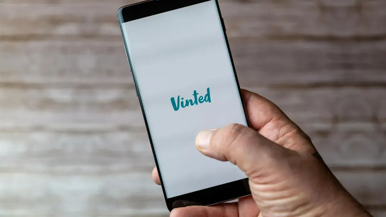 Dłoń trzyma smartfon z logo Vinted. Planuję odbiór osobisty zakupionych ubrań.