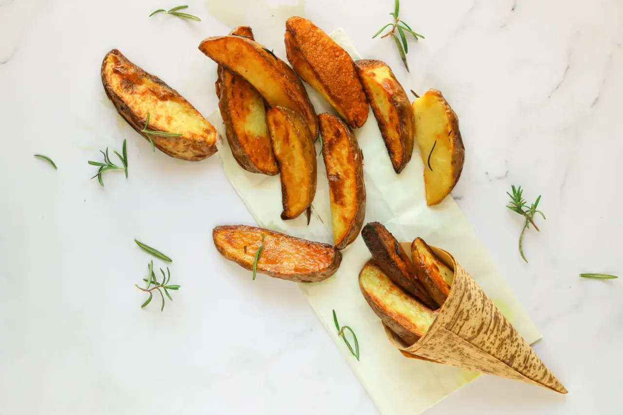 Patate al forno dorate e croccanti, profumate al rosmarino, servite su carta da forno e in un cono di bambù.