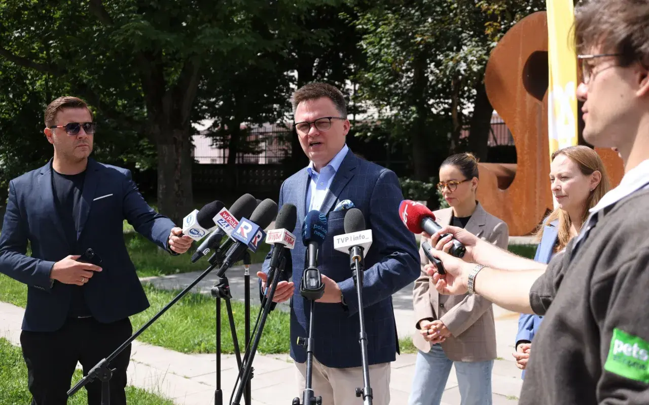 Wpływ social mediów i podcastów na popularność Polska 2050: polityk przemawia do mediów, otoczony mikrofonami.