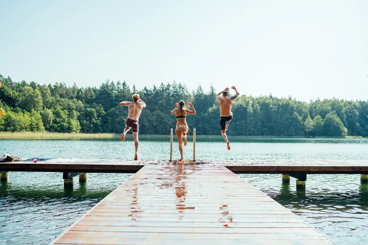 Drei Freunde springen von einem Steg in den See der Mecklenburgischen Seenplatte. Ein perfekter Sommertag am mecklenburgische seenplatte strand.