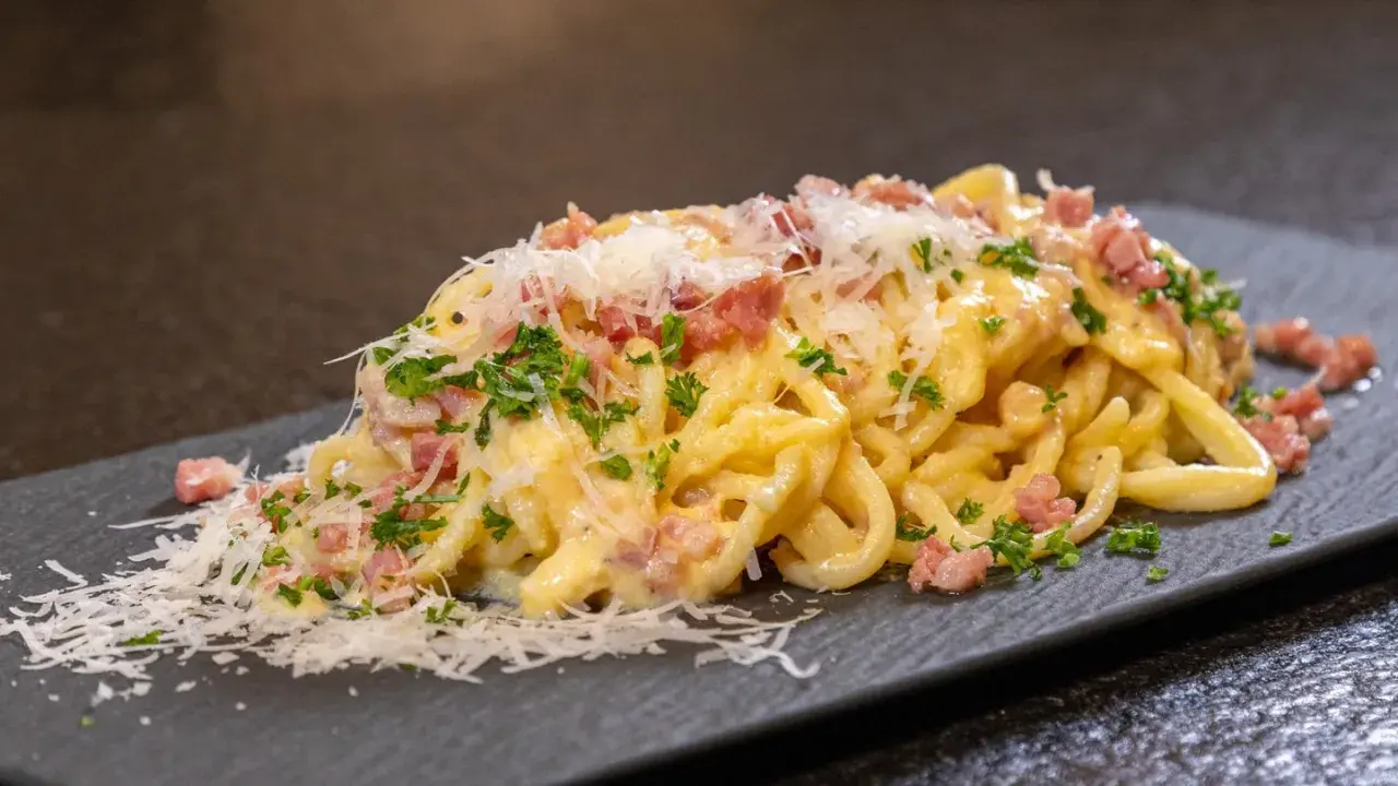 Eine Portion echte Carbonara mit cremiger Sauce, Guanciale und frisch geriebenem Parmesan auf einem dunklen Teller.