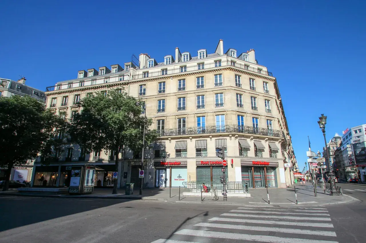 Elegancka kamienica przy rue de Rivoli w Paryżu, z markizami nad oknami i sklepem Foot Locker na parterze.