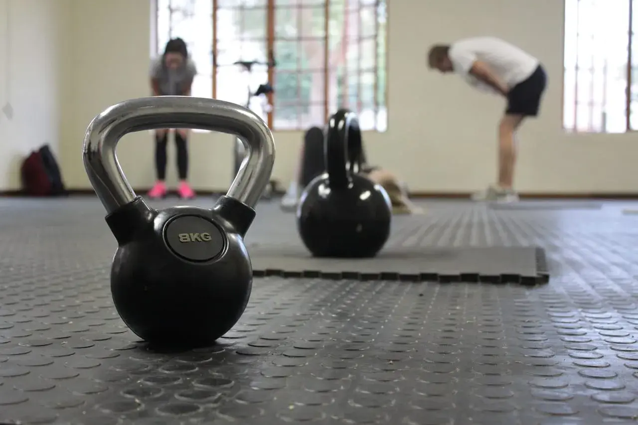 Kettlebell 8kg na siłowni, w tle ćwiczący ludzie.